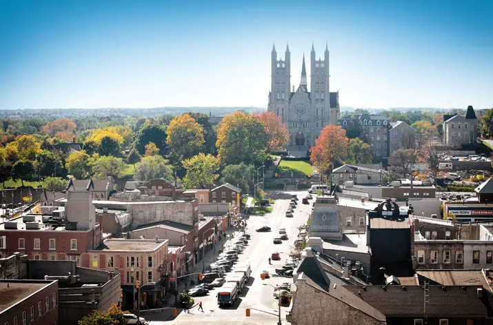 An aerial view of the downtown of the city of guelph in ontario. A church with two towers stands on a hill above the downtown shops and streets