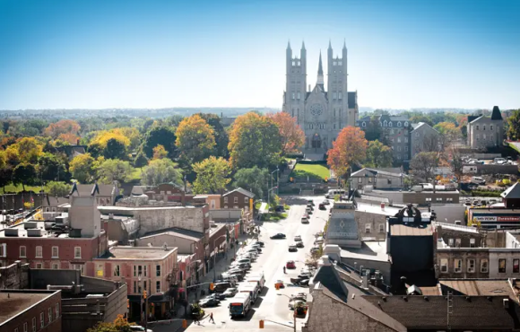 An aerial view of the downtown of the city of guelph in ontario. A church with two towers stands on a hill above the downtown shops and streets